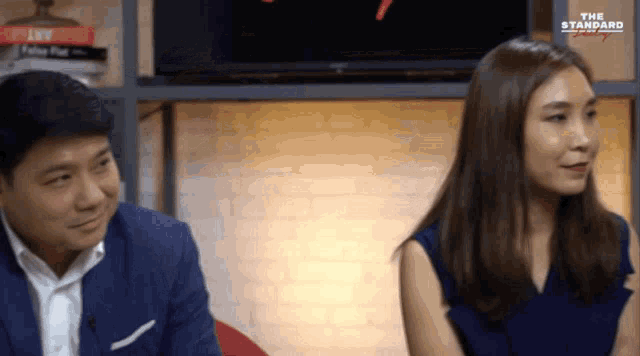 a man and a woman are sitting in front of a screen that says " the standard "