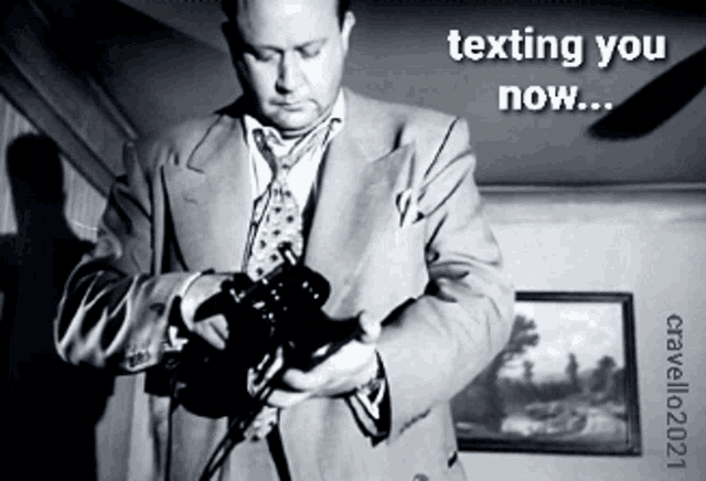 a man in a suit and tie is holding a camera with the words texting you now written above him