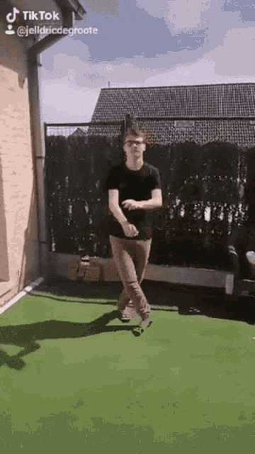 a man in a black shirt is dancing on a green lawn with a tik tok watermark