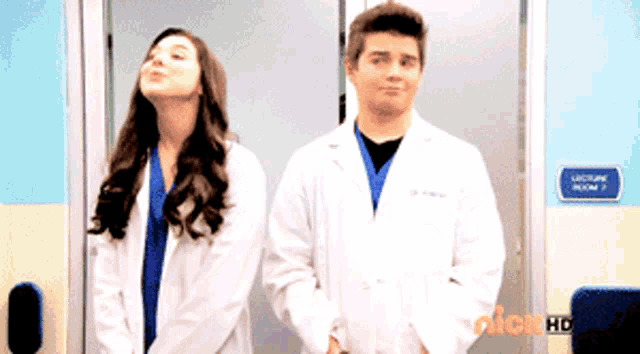 a man and a woman in lab coats stand in front of a lecture room sign