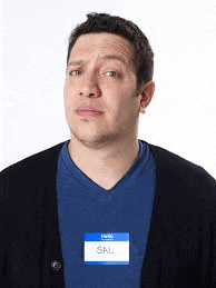 a man wearing a blue shirt and a black cardigan has a name tag on his neck .