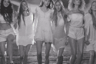 a group of women in white dresses and shorts are walking down a street holding hands .