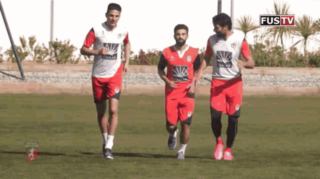 three soccer players are running on a field with the words fustv in the corner
