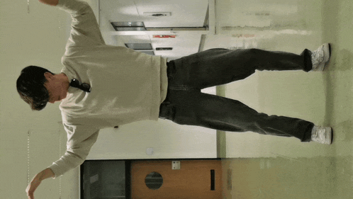 a man standing in a hallway with his arms outstretched and a door with a round window