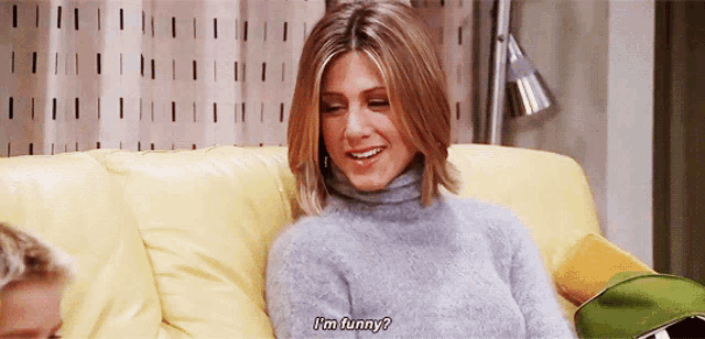 a woman in a grey sweater is sitting on a yellow couch and saying i 'm funny ?