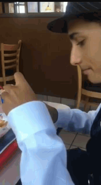 a man wearing a hat is sitting at a table with his hand on his wrist