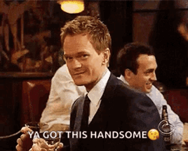 a man in a suit and tie is sitting at a table in a restaurant holding a glass of wine .
