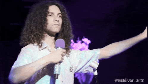 a man with long curly hair is holding a purple microphone in front of a purple background