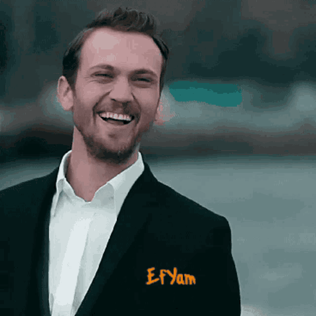 a man in a suit and white shirt is smiling with the name efyan on his pocket