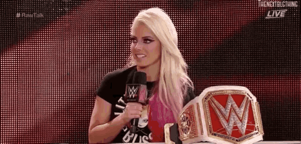 a woman is talking into a microphone while holding a wwe championship belt .