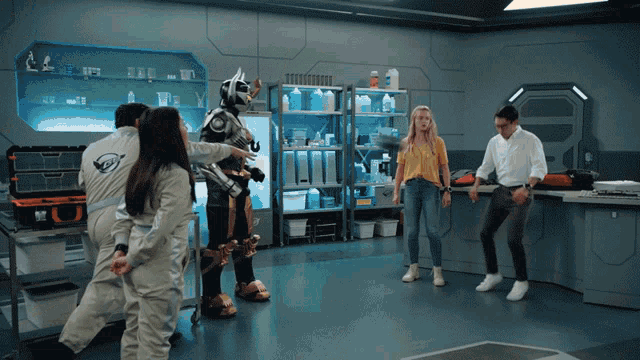a group of people are standing around a robot in a room with shelves of bottles