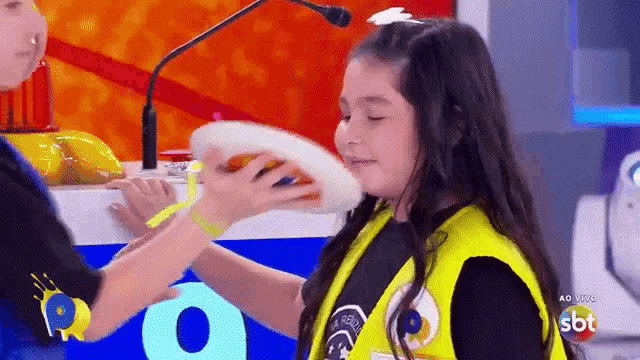 a girl in a yellow vest is being given a pizza by another girl