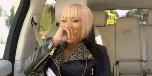 a woman with blonde hair is sitting in the back seat of a car covering her mouth .