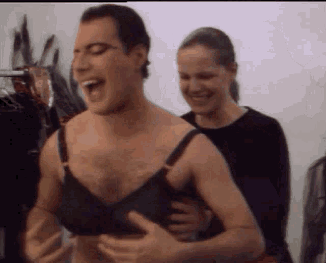 a man wearing a bra is laughing while a woman holds his chest