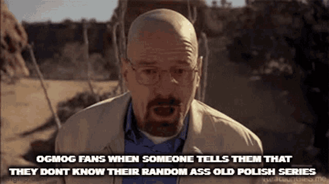 a bald man with glasses and a beard is standing in a desert talking to someone .