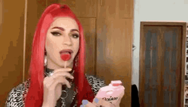 a drag queen with red hair is eating a lollipop and holding a bottle of milk .