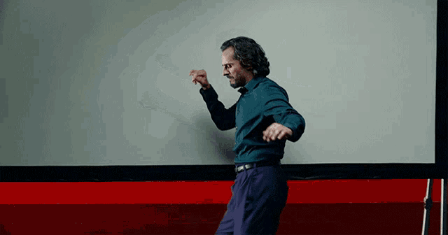 a man in a blue shirt is dancing in front of a white wall