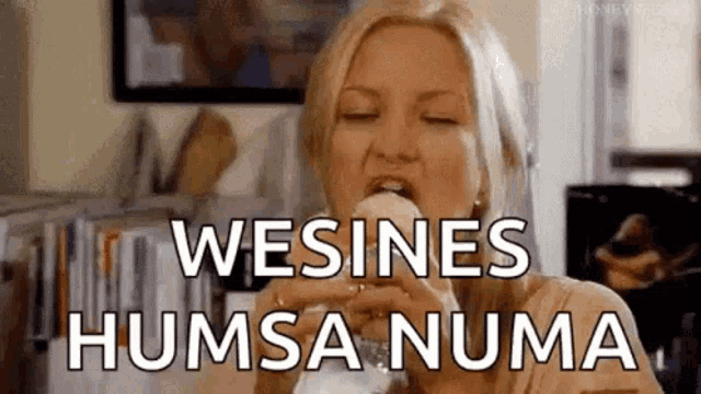 a woman is eating a sandwich with the words wesines humsa numa written on it .