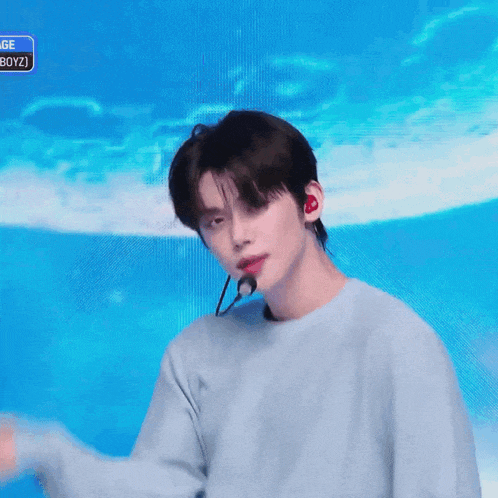 a young man wearing a light blue sweater and a microphone is standing in front of a blue background .
