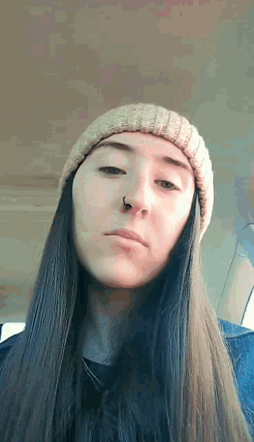 a woman with long hair and a nose ring is wearing a beanie