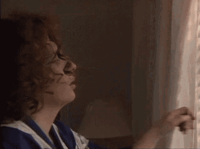 a woman in a blue and white striped shirt is looking out of a window