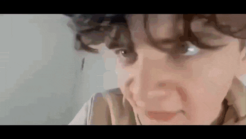 a close up of a person 's face with curly hair looking at the camera .