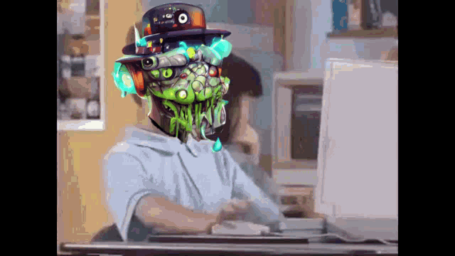 a person is sitting at a desk with a computer and a robot head on their head .