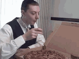 a man is sitting at a table eating pizza from a box .