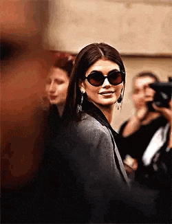a woman wearing sunglasses and earrings is walking down a street .
