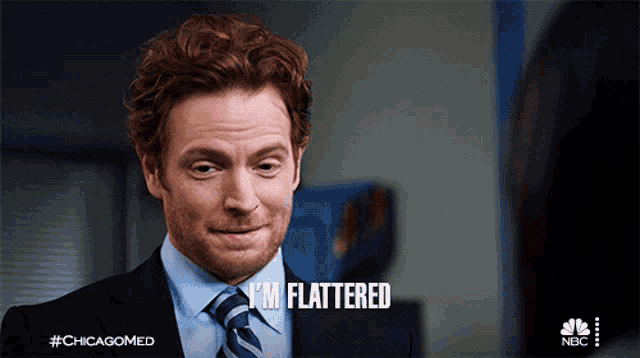 a man in a suit and tie says " i 'm flattered " on the screen