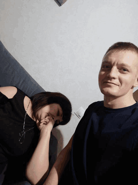 a man and a woman are sitting on a couch and the woman is covering her face with her hand