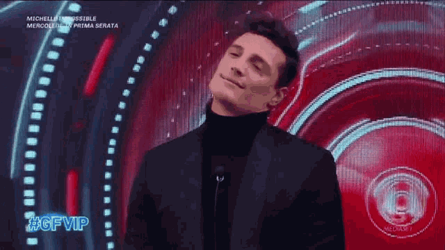 a man in a suit and turtleneck is smiling in front of a screen that says gf vip