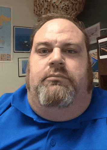 a man with a beard wearing a blue shirt is looking at the camera