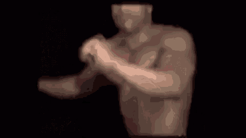a man without a shirt is standing in a dark room with his arms outstretched .
