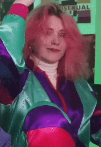 a woman with pink hair stands in front of a wall with a sexual sign on it