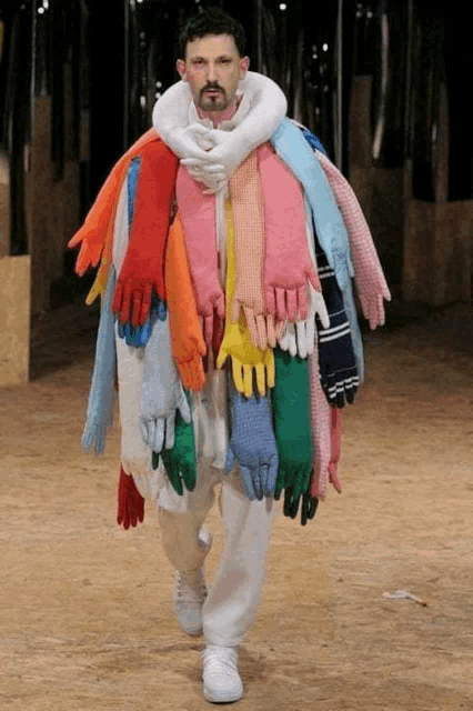 a man is walking down a runway wearing a lot of colorful gloves