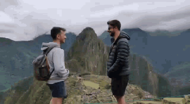 two men standing next to each other on top of a mountain .