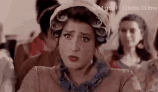 a woman with curlers in her hair is making a funny face in front of a crowd .