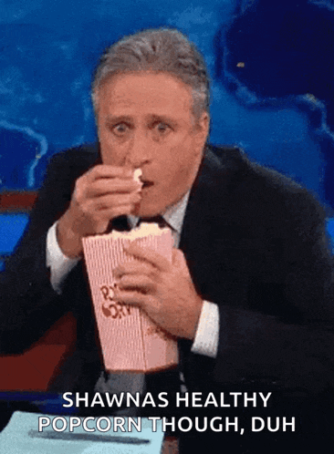 a man in a suit and tie is eating popcorn and says shawnas healthy popcorn though duh