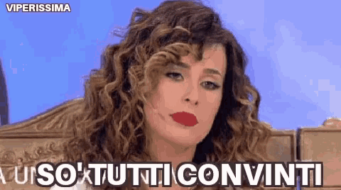 a woman with curly hair and red lipstick is sitting in front of a sign that says " viperissima "