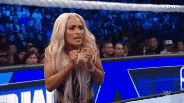 a woman is standing in front of a crowd in a wrestling ring with her hands in her pockets .