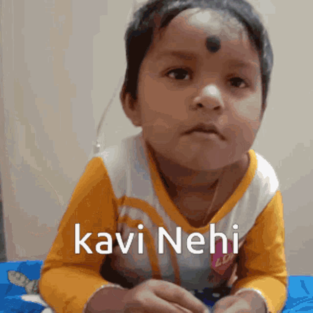 a little girl with a bindi on her forehead is wearing a yellow and white shirt that says kavi nehi