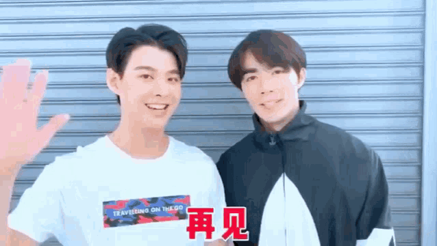 two young men are standing next to each other in front of a garage door and waving at the camera .