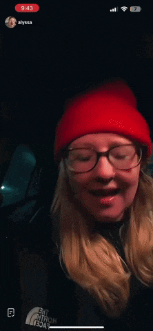 a woman wearing glasses and a red hat is laughing on a video call