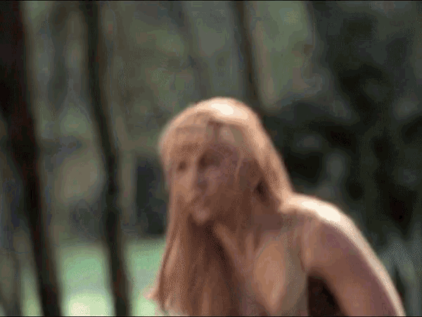 a woman with long hair is standing in the woods .