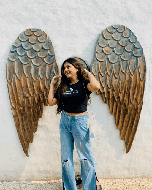 a woman stands in front of a wall with angel wings