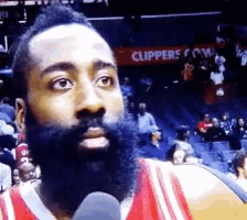 a man with a beard is talking into a microphone with a clippers sign in the background