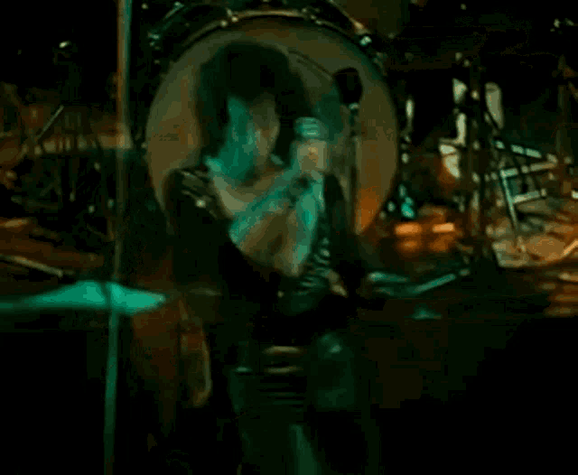 a man is playing a guitar and singing into a microphone while standing in front of a drum set .