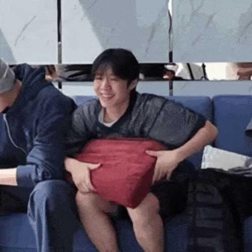 a man and a woman are sitting on a couch holding a red pillow .