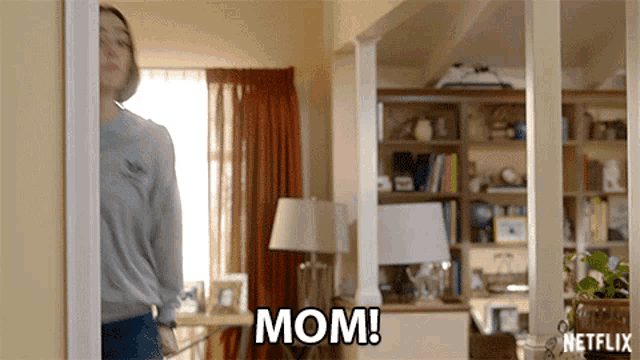 a woman is standing in a living room with the word mom written on the wall